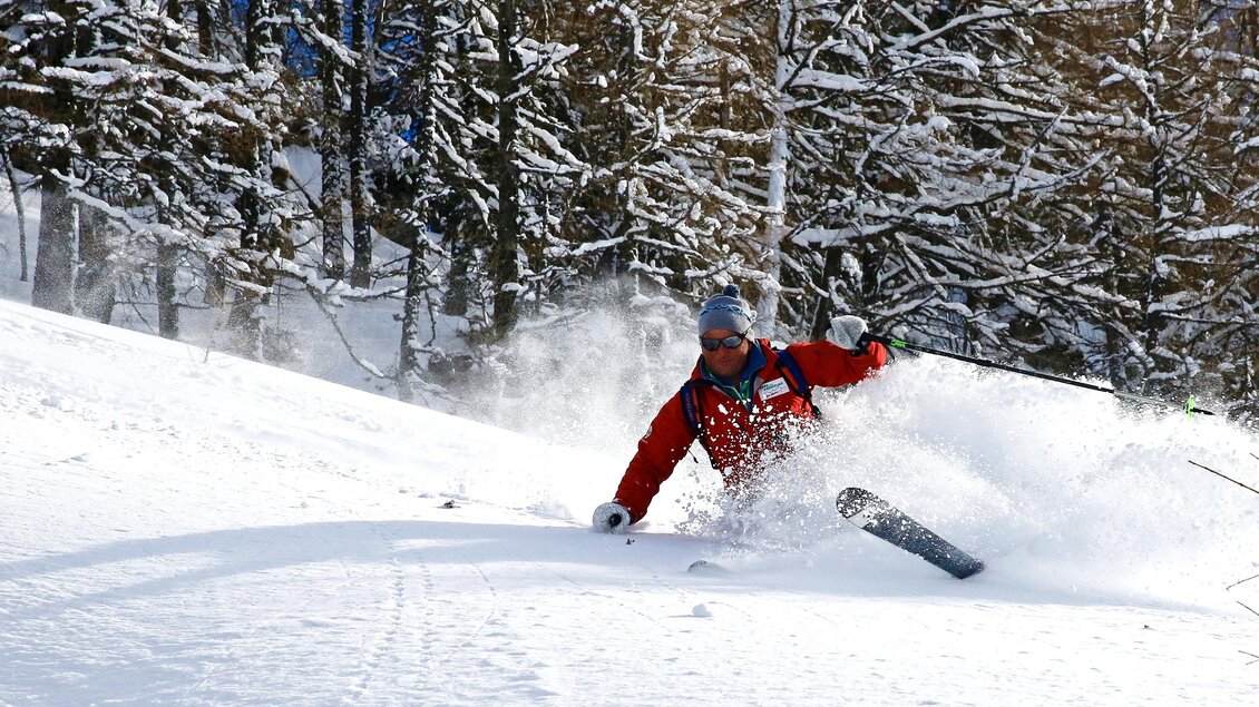 Ein Skifahrer in roter Kleidung macht eine Kurve im frischen Schnee. Im Hintergrund sind verschneite Bäume sichtbar. | © Heli Rettensteiner
