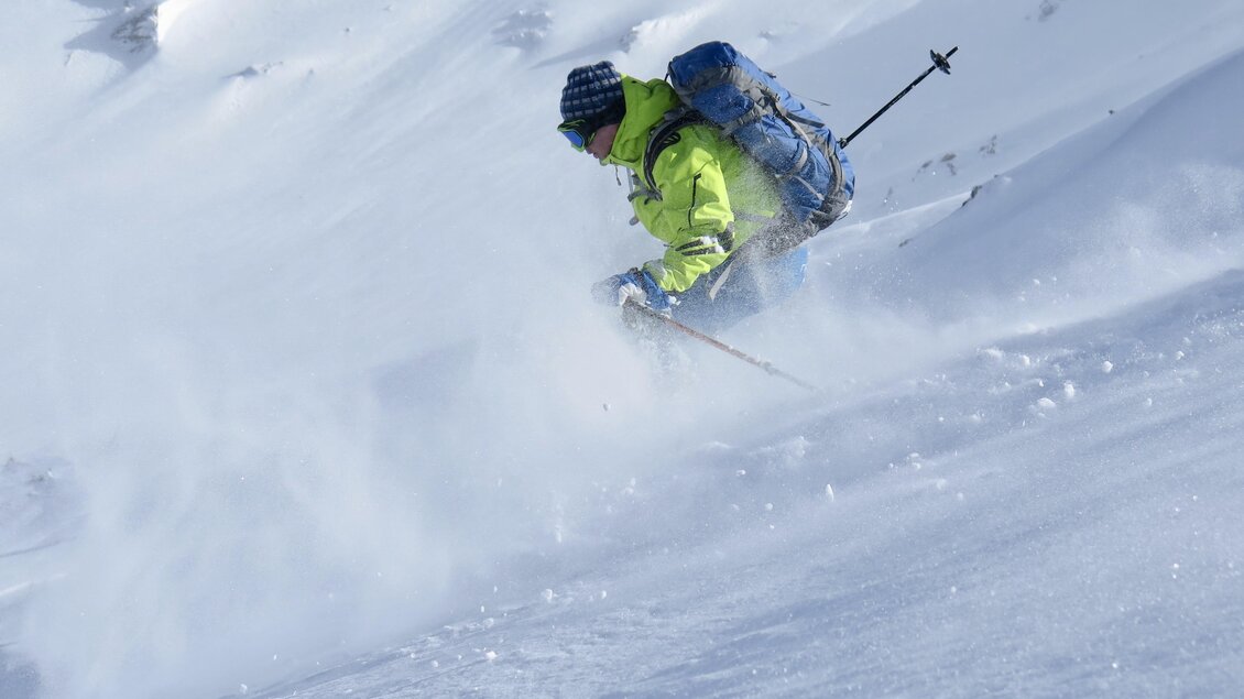 Ein Skifahrer fährt durch frischen Schnee in einer winterlichen Landschaft. Der klare Himmel und die verschneiten Berge schaffen eine beeindruckende Kulisse. | © Heli Rettensteiner