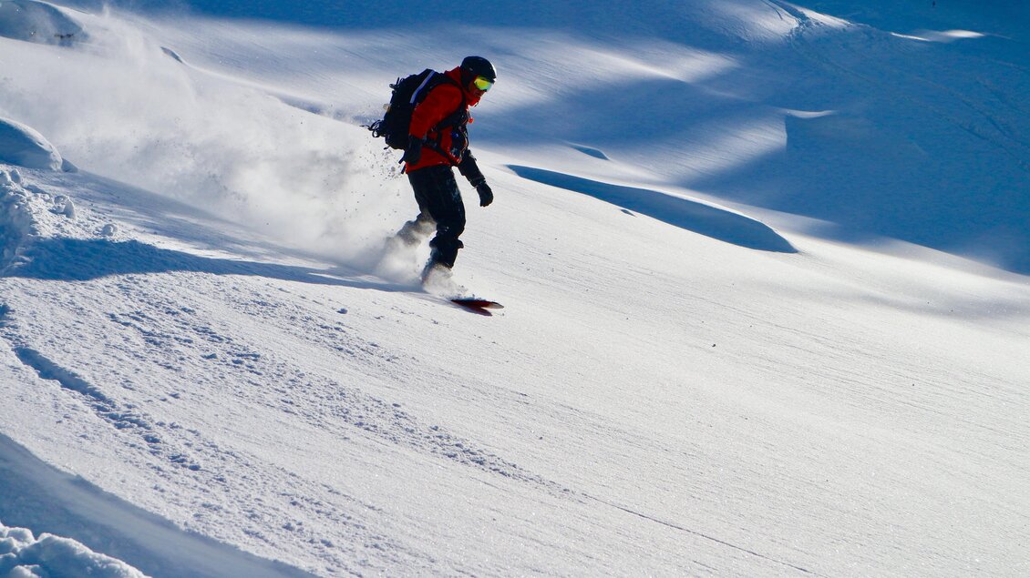 Ein Snowboarder fährt durch tiefen Schnee. Die Umgebung ist winterlich und sonnig. | © Heli Rettensteiner