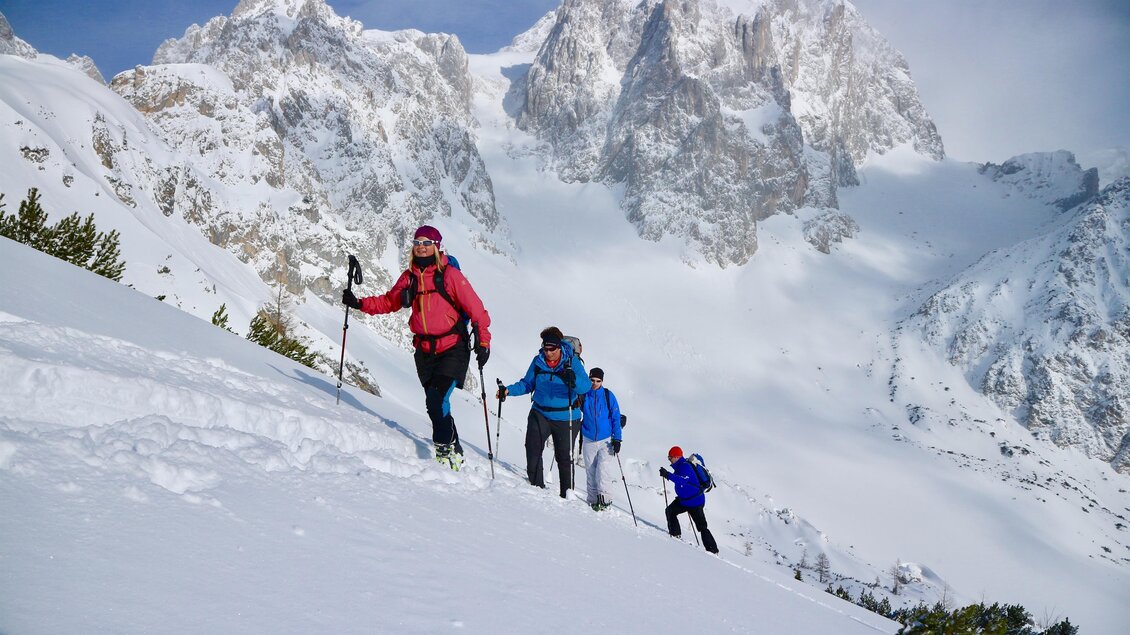 Eine Gruppe von Menschen wandert in den schneebedeckten Bergen. Im Hintergrund sind hohe, majestätische Felsen und blauer Himmel zu sehen. | © Heli Rettensteiner