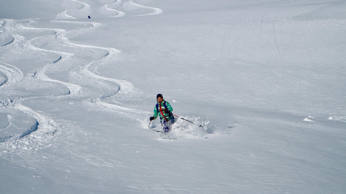 Ein Skifahrer fährt durch unberührten Schnee und hinterlässt Spuren im weißen Gelände. Die Sonne scheint auf die winterliche Landschaft. | © Heli Rettensteiner