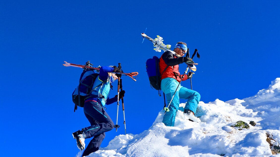 Zwei Bergsteiger steigen in die verschneite Berglandschaft. Der Himmel ist klar und blau, und sie tragen passende Ausrüstung. | © Heli Rettensteiner