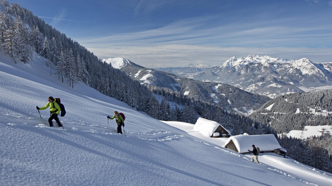Zwei Wanderer steigen einen schneebedeckten Hügel hinauf. Im Hintergrund sind schneebedeckte Berge und eine klare Blauen Himmel zu sehen. | © Herbert Raffalt