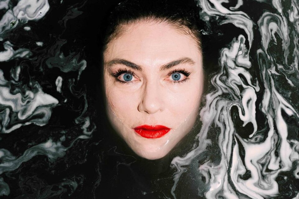 Eine Frau mit auffälligen blauen Augen und roten Lippen steht in einer dunkel gefärbten, schaumigen Flüssigkeit. Der Kontrast zwischen ihrem Gesicht und dem Hintergrund erzeugt eine faszinierende Atmosphäre. | © Ingo Pertramer- Oper Graz