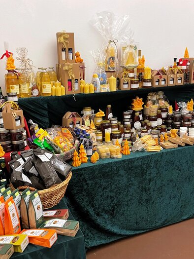 A colorful market stall with various bottles, honey, jam, and snacks. The goods are attractively displayed and invite you to sample them. | © TV Thermen- & Vulkanland