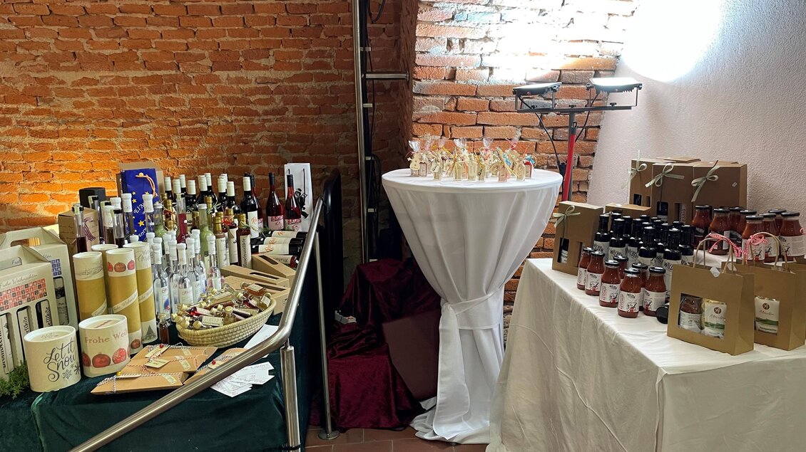 Ein Verkaufsstand mit verschiedenen Flaschen und Gläsern auf den Tischen. Im Hintergrund sind Ziegelwände und warmes Licht zu sehen. | © TV Thermen- & Vulkanland