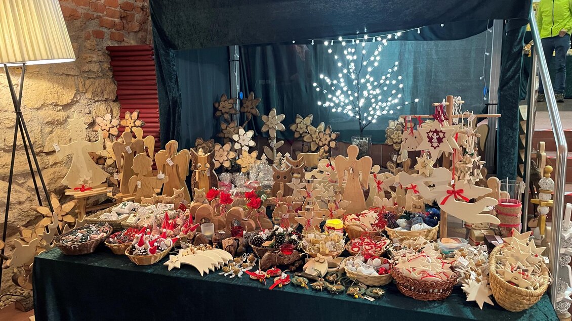 Ein festlich dekorierter Tisch mit handgemachten Holzfiguren und verschiedenen Leckereien. Im Hintergrund glitzern Lichter, die eine warme Atmosphäre schaffen. | © TV Thermen- & Vulkanland