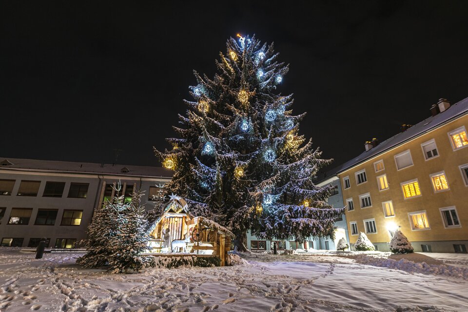 Ein großer, festlich beleuchteter Weihnachtsbaum steht im Schnee. Im Hintergrund sind mit Lichtern dekorierte Gebäude zu sehen. | © Tourismus Murtal-Anita Fössl
