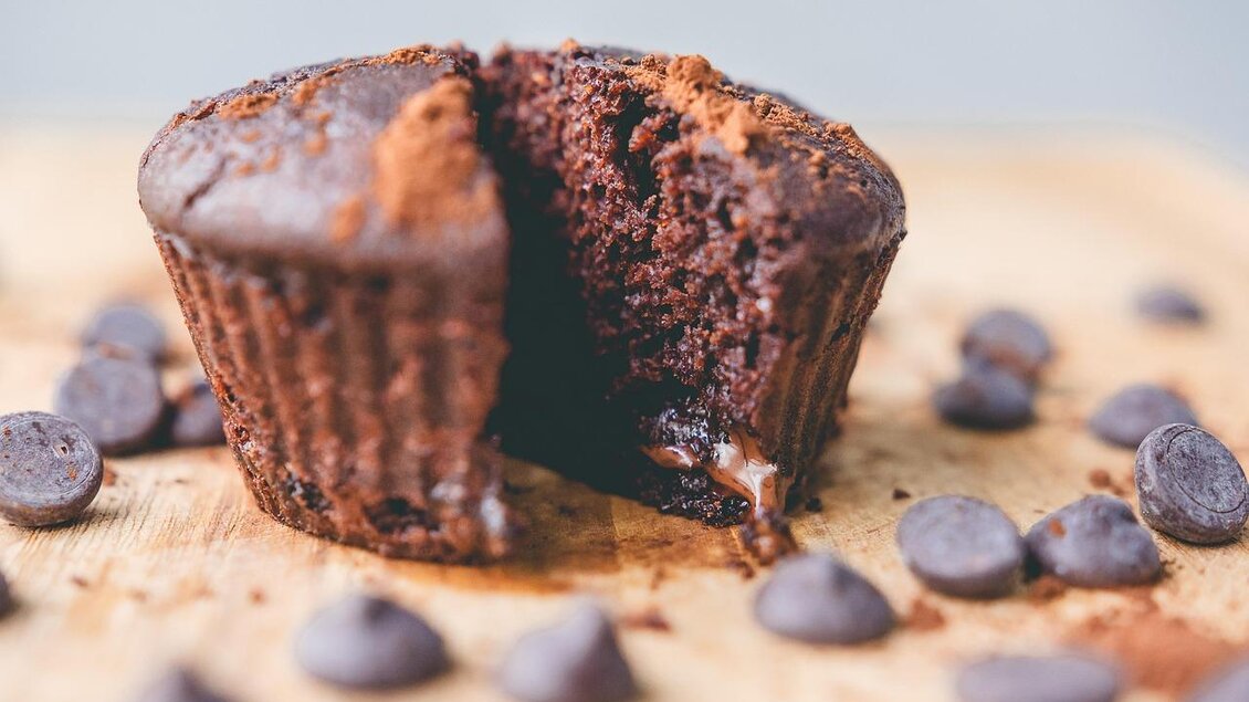 Ein leckerer Schokoladenmuffin, der halbiert ist, zeigt flüssige Schokolade im Inneren. Rundherum liegen Schokoladendrops. | © Pixabay