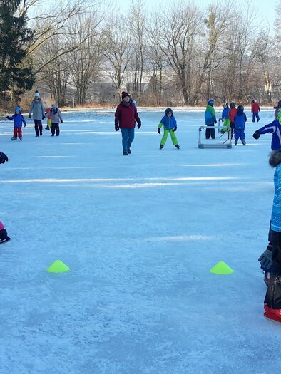 Eine Gruppe von Kindern läuft auf einem zugefrorenen See Schlittschuh. Im Hintergrund sind Erwachsene und weitere Kinder zu sehen, umgeben von schneebedeckten Bäumen. | © Volksschule Bad Waltersdorf