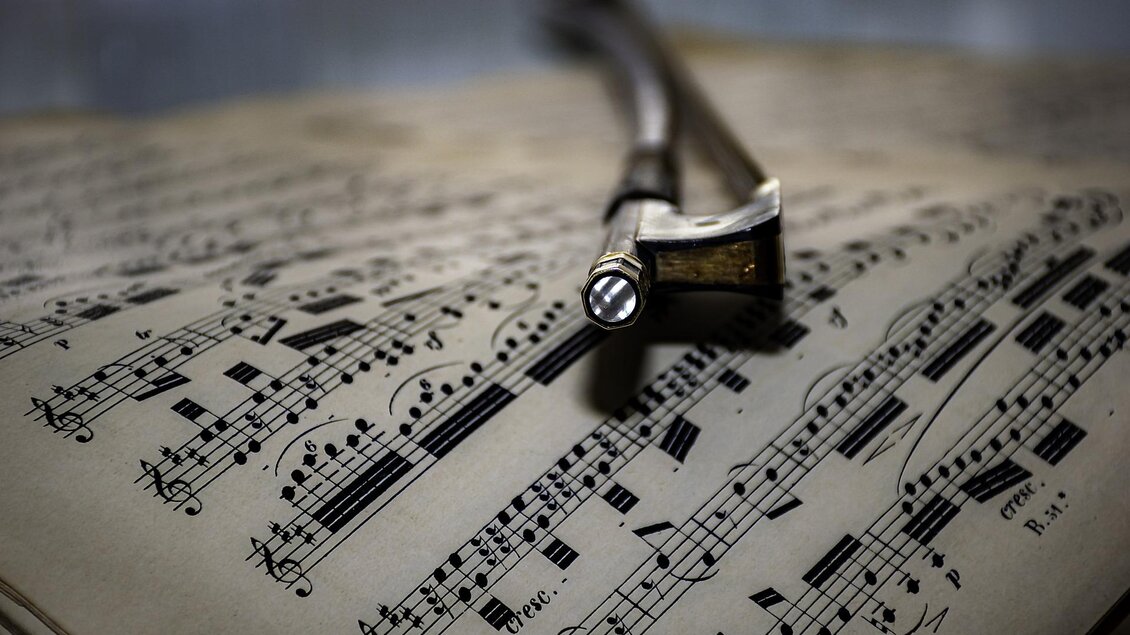 Ein Bogen liegt auf einem geöffneten Notenblatt. Die Noten sind klar und deutlich auf dem Papier abgebildet. | © Symbolfoto Pixabay