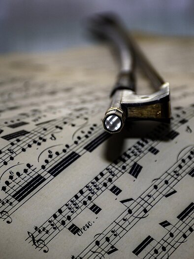 Ein Bogen liegt auf einem geöffneten Notenblatt. Die Noten sind klar und deutlich auf dem Papier abgebildet. | © Symbolfoto Pixabay