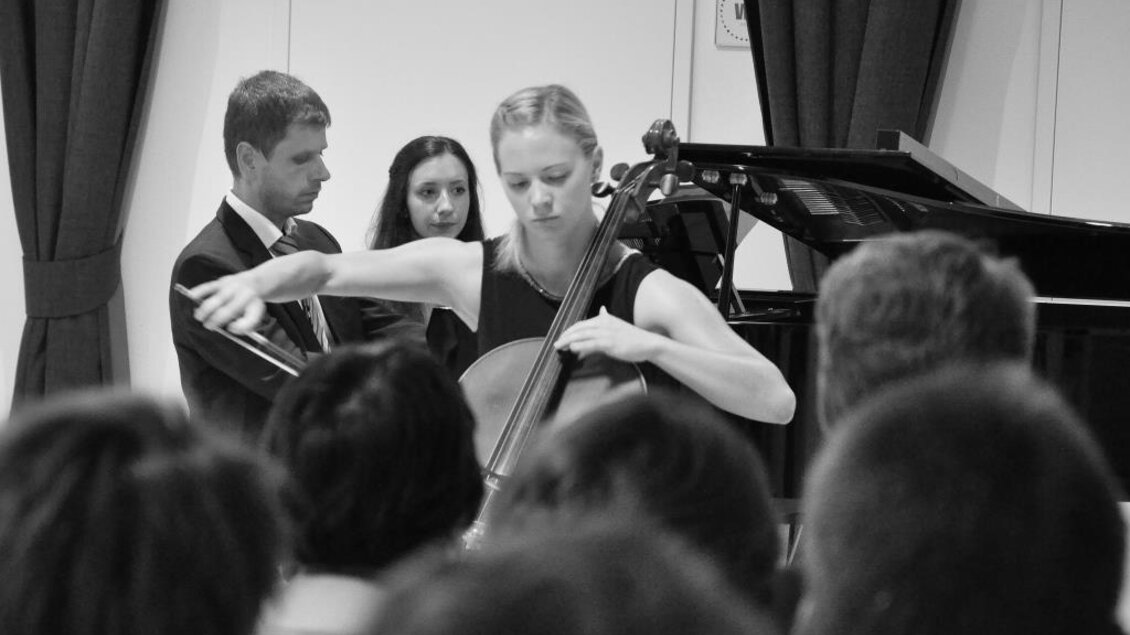 Eine Cellistin spielt vor einem Publikum. Im Hintergrund sind ein Pianist und eine Zuhörerin zu sehen. | © Kulturreferat der Marktgemeinde Irdning-Donnersbachtal