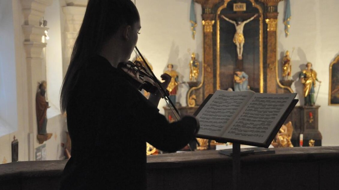 Eine junge Frau spielt Geige in einer Kirche. Im Hintergrund sind religiöse Figuren und ein Kreuz zu sehen. | © Kulturreferat der Marktgemeinde Irdning-Donnersbachtal