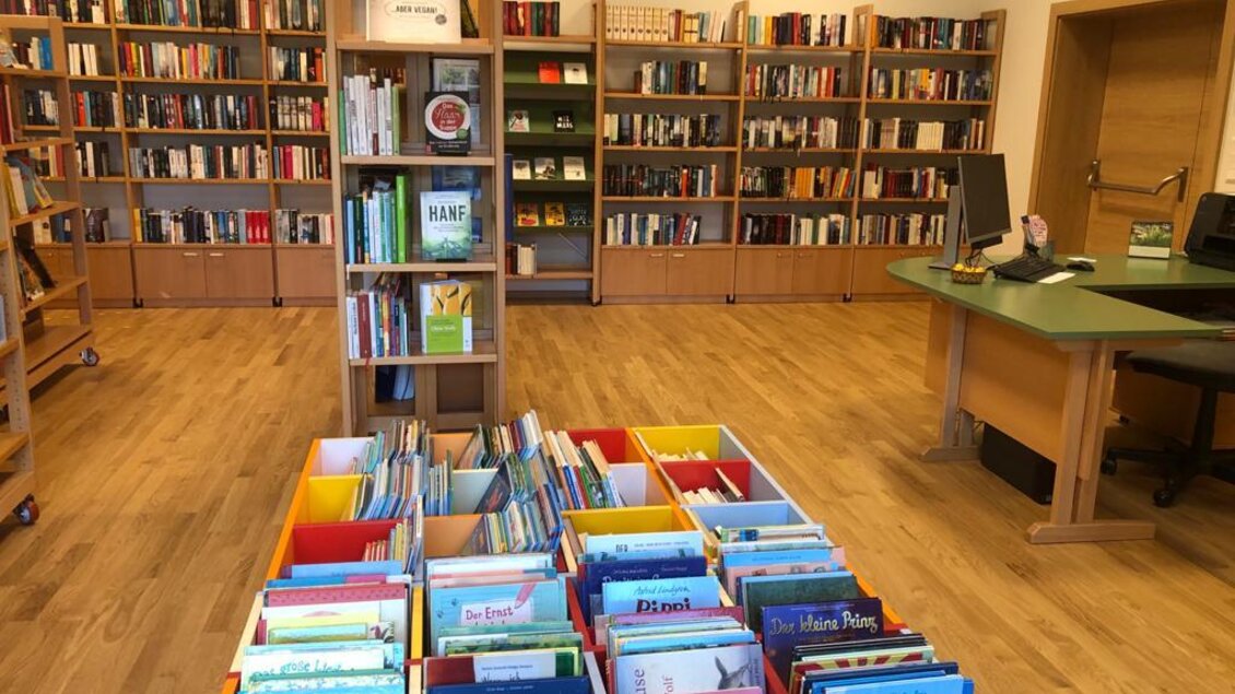 Ein gemütlicher Raum mit vielen Bücherregalen. In der Mitte stehen Kisten mit bunten Kindermagazinen und -büchern. | © Gemeinde Bad Waltersdorf