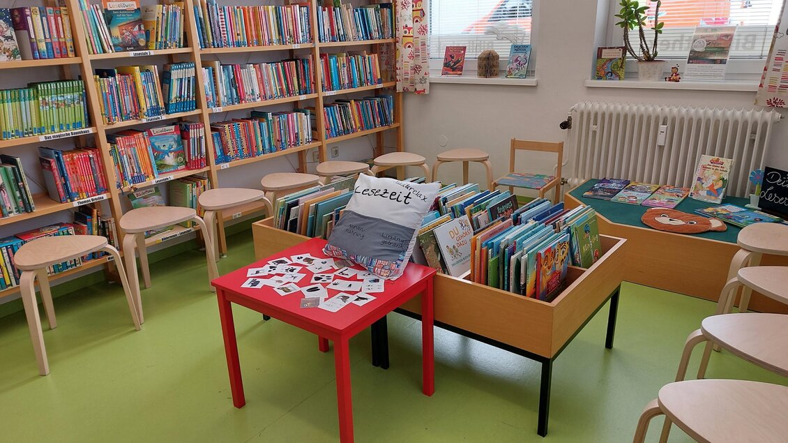 Ein angenehmer Raum mit Regalen voller Bücher und einem Tisch mit verschiedenen Kinderbüchern. Stühle stehen bereit für Lesestunden oder Aktivitäten. | © Öffentliche Bibliothek der MG Stainach-Pürgg