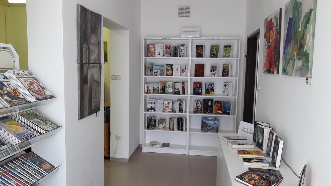Ein heller Raum mit Regalen voller Bücher und Zeitschriften. An der Wand hängen einige Kunstwerke in verschiedenen Farben. | © Bibliothek der MG Stainach-Pürgg