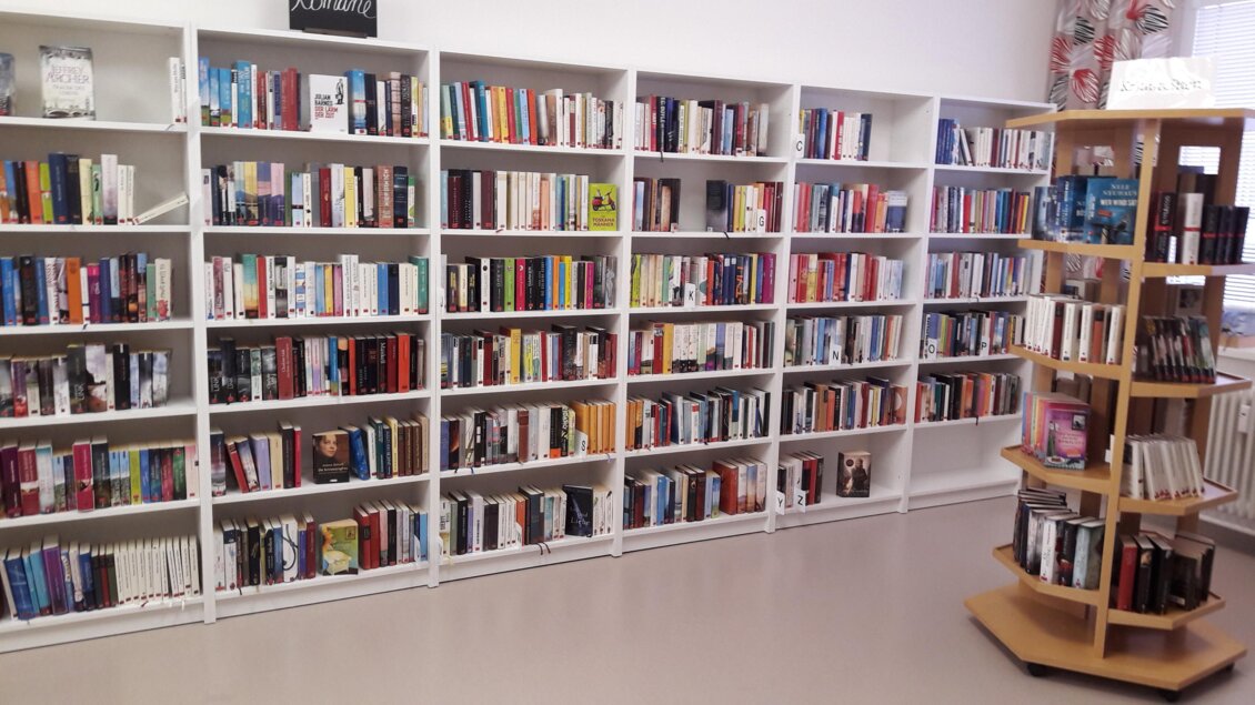 Ein Raum mit weißen Bücherregalen voller Bücher. In der Mitte steht ein runder Bücherständer. | © Bibliothek der MG Stainach-Pürgg