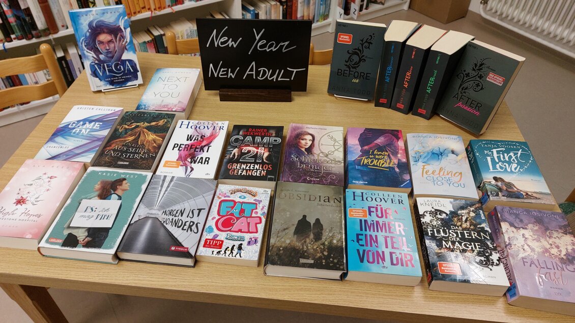 Ein Tisch voller Bücher, die vielfältige Geschichten für junge Erwachsene bieten. Ein Schild mit der Aufschrift "New Year, New Adult" steht im Hintergrund. | © ÖB der MG Stainach-Pürgg