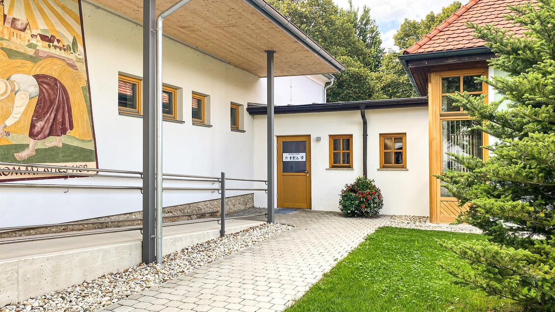 Ein moderner Eingang mit einer gepflasterten Auffahrt und einem gepflegten Garten. An der Wand ist ein künstlerisches Wandbild zu sehen. | © TVB Bad Waltersdorf