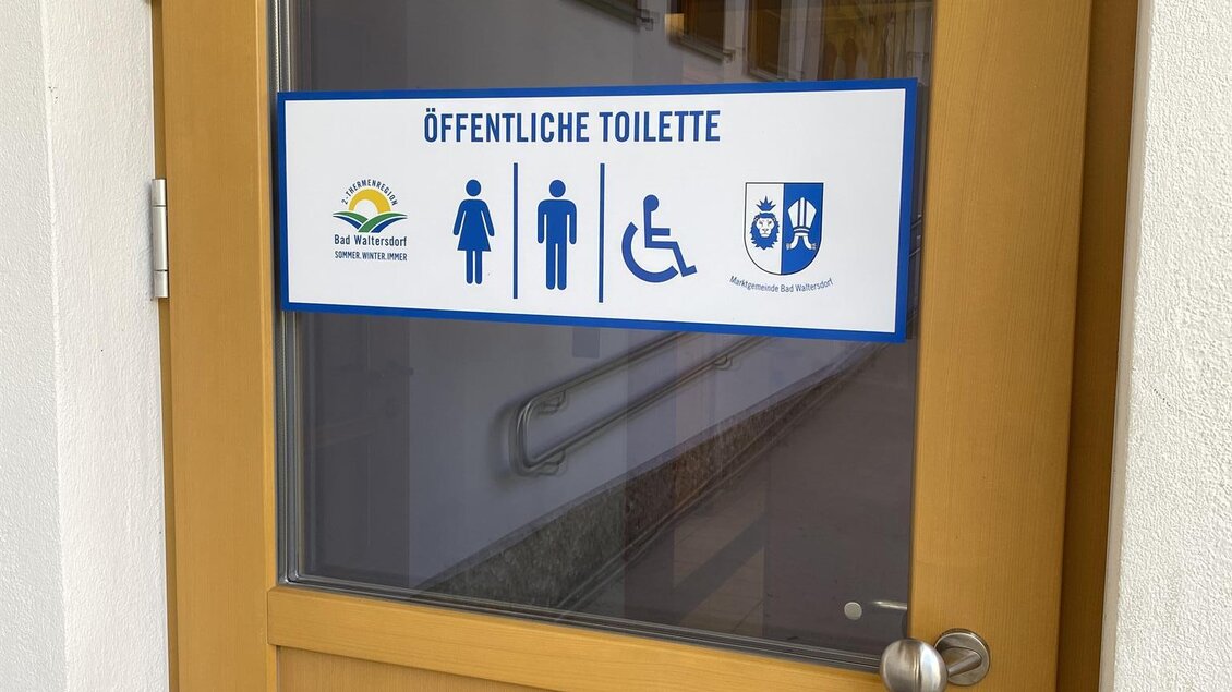 Die Tür zu einer öffentlichen Toilette ist sichtbar. Ein Schild zeigt Symbole für Männer, Frauen und barrierefreien Zugang. | © TVB Bad Waltersdorf