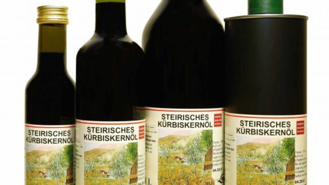 Mehrere Flaschen und Dosen mit steirischem Kürbiskernöl sind auf einem weißen Hintergrund abgebildet. Das Design der Etiketten zeigt eine ländliche Szene und die Aufschrift „Steirisches Kürbiskernöl“. | © Ölmühle Lugitsch