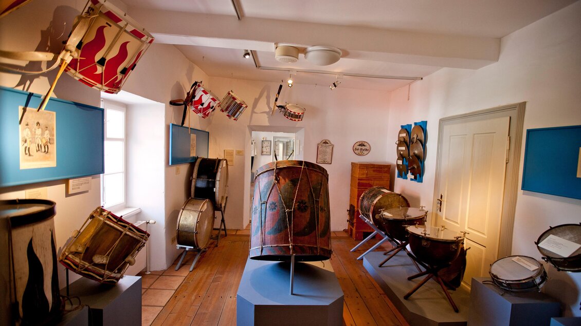 Ein Musikinstrumentenmuseum mit verschiedenen Trommeln. Die Wände sind geschmückt mit alten Fahnen und Bildern. | © Holzwelt Murau