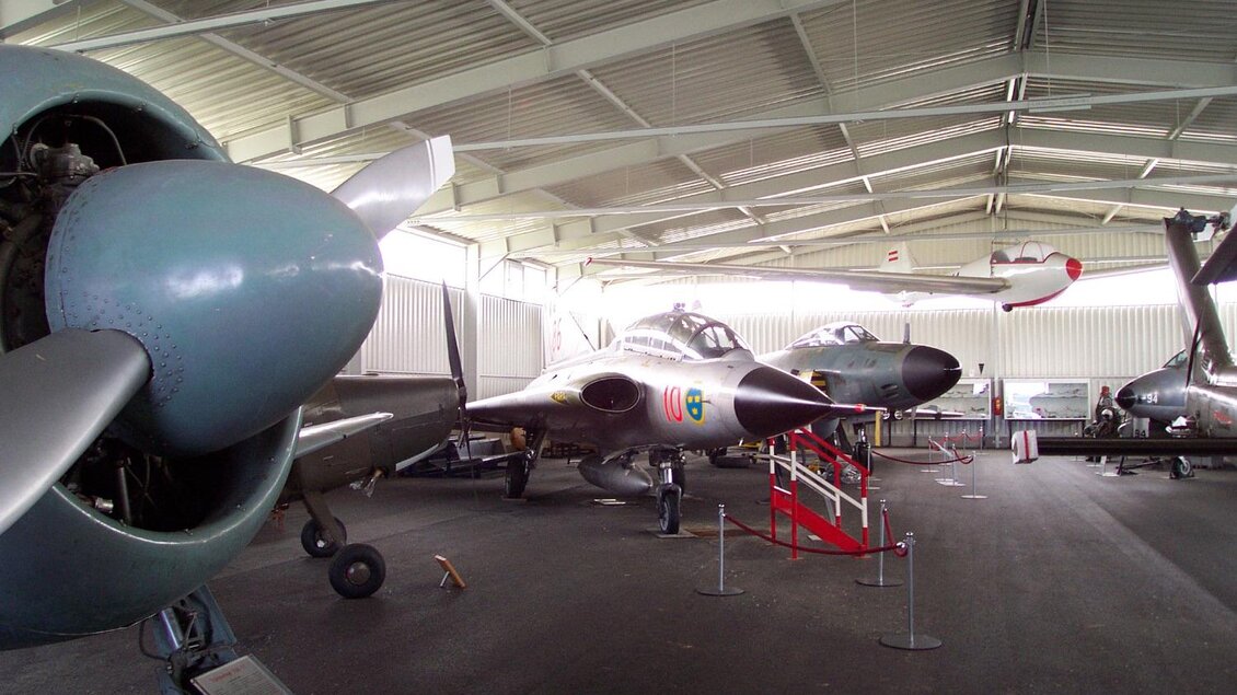 Eine Sammlung von historischen Flugzeugen in einem großen Hangar. Zu sehen sind verschiedene Flugzeugmodelle und Propeller. | © Österreichisches Luftfahrtmuseum