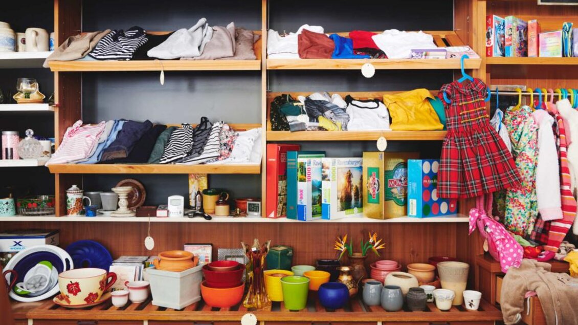 Ein gut sortierter Secondhand-Laden mit Kleidung auf Regalen und verschiedenen Haushaltsgegenständen. Auf der unteren Ebene sind bunte Töpfe und Spielzeuge zu sehen. | © Verein ALH