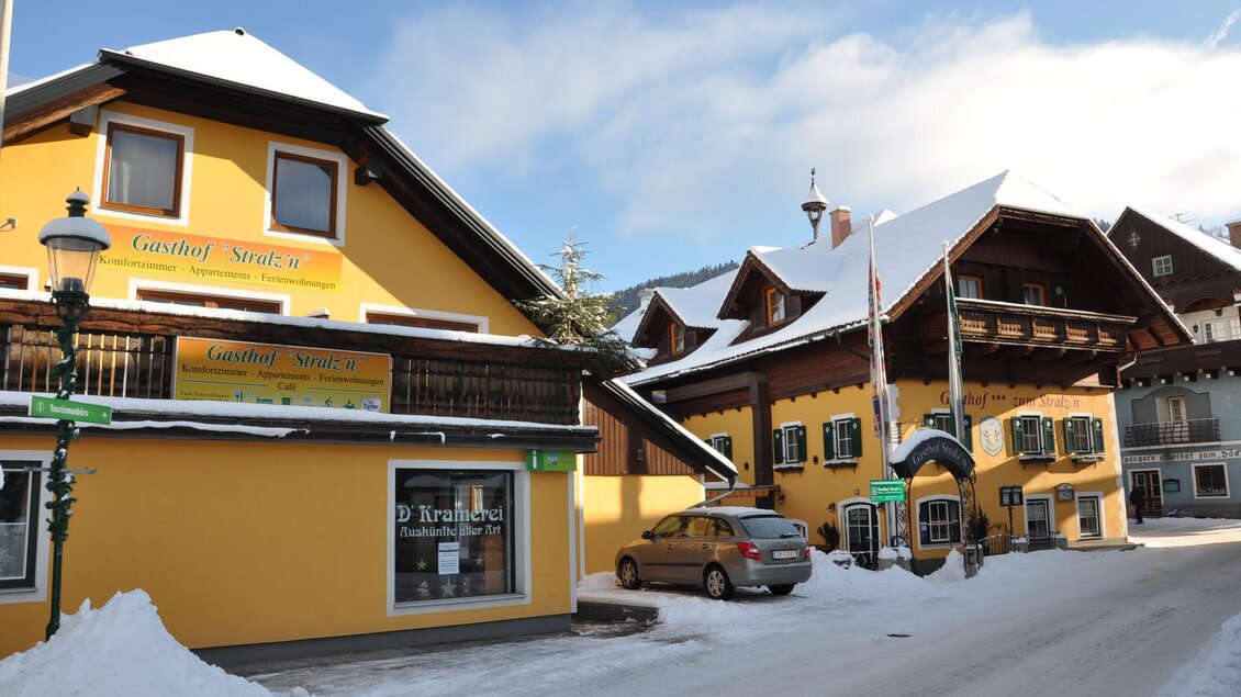 Ein malerisches Dorfhaus mit gelber Fassade und verschneiten Dächern. Die Straße ist schneebedeckt und von gemütlichen Gebäuden gesäumt. | © Gerhard Schernthaner
