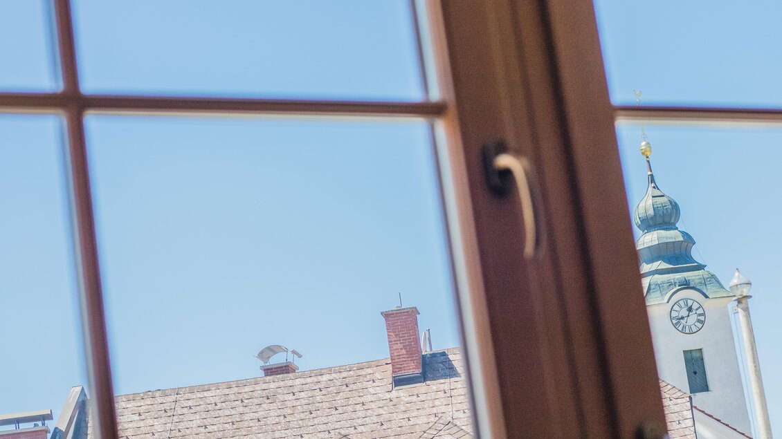 Blick aus einem Fenster auf Dächer und einen Kirchturm. Der Himmel ist klar und blau. | © Gerhard Schernthaner