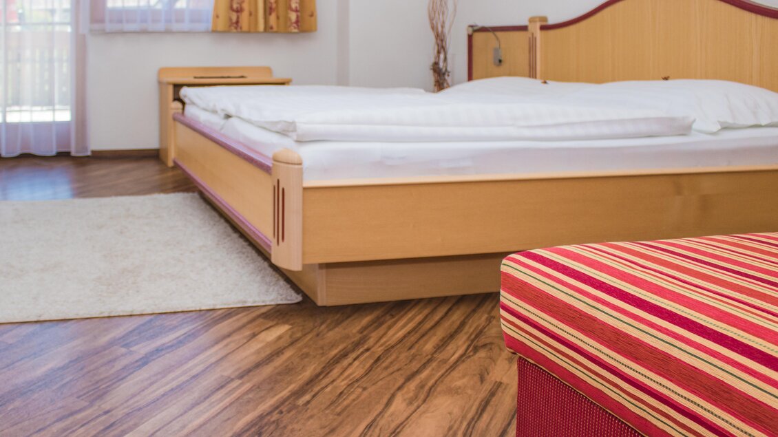 Ein modernes Schlafzimmer mit einem großen Bett und einem roten Streifensofa. Der Raum hat Holzfußboden und große Fenster, die natürliches Licht hineinlassen. | © Gerhard Schernthaner