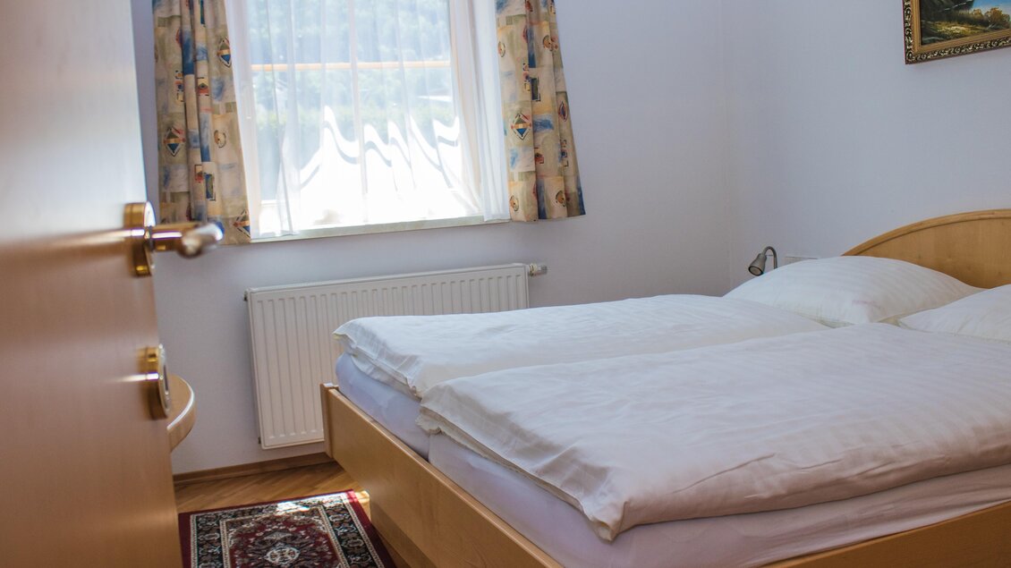 Ein gemütliches Schlafzimmer mit einem Doppelbett und heller Einrichtung. Das Zimmer ist freundlich beleuchtet und hat ein Fenster mit Vorhängen. | © Gerhard Schernthaner