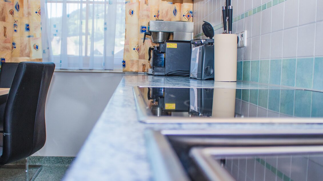 Eine moderne Küche mit glänzenden Oberflächen und einem klaren Fenster. Auf der Arbeitsplatte sind verschiedene Küchengeräte zu sehen. | © Gerhard Schernthaner