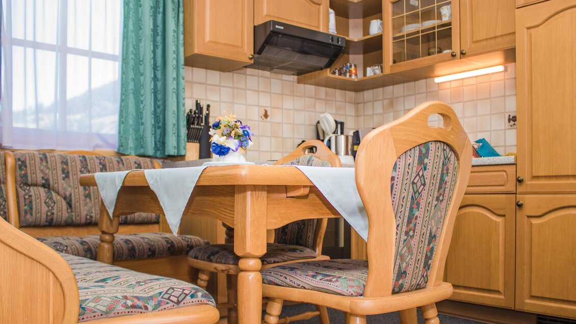 Eine gemütliche Küche mit Holzmöbeln und einem Tisch, der für eine Mahlzeit gedeckt ist. Im Hintergrund sind Küchenschränke und verschiedene Küchengeräte zu sehen. | © Gerhard Schernthaner