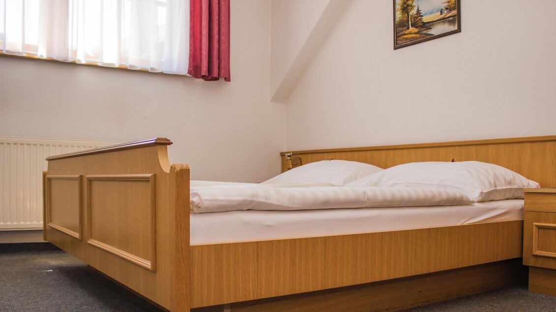 Ein einfaches Schlafzimmer mit einem Holzbett und zwei Kissen. Die Fenster lassen viel Tageslicht herein und ein Gemälde hängt an der Wand. | © Gerhard Schernthaner