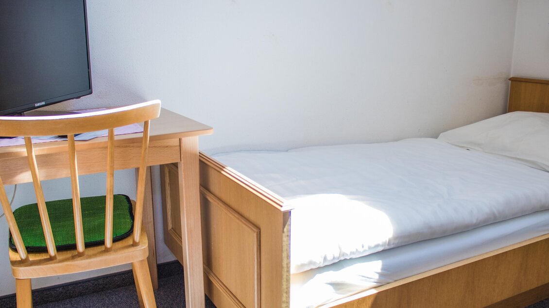 Ein einfaches Zimmer mit einem Einzelbett und einem Schreibtisch. Ein Fernseher steht auf dem Tisch, und viel Tageslicht fällt durch das Fenster. | © Gerhard Schernthaner