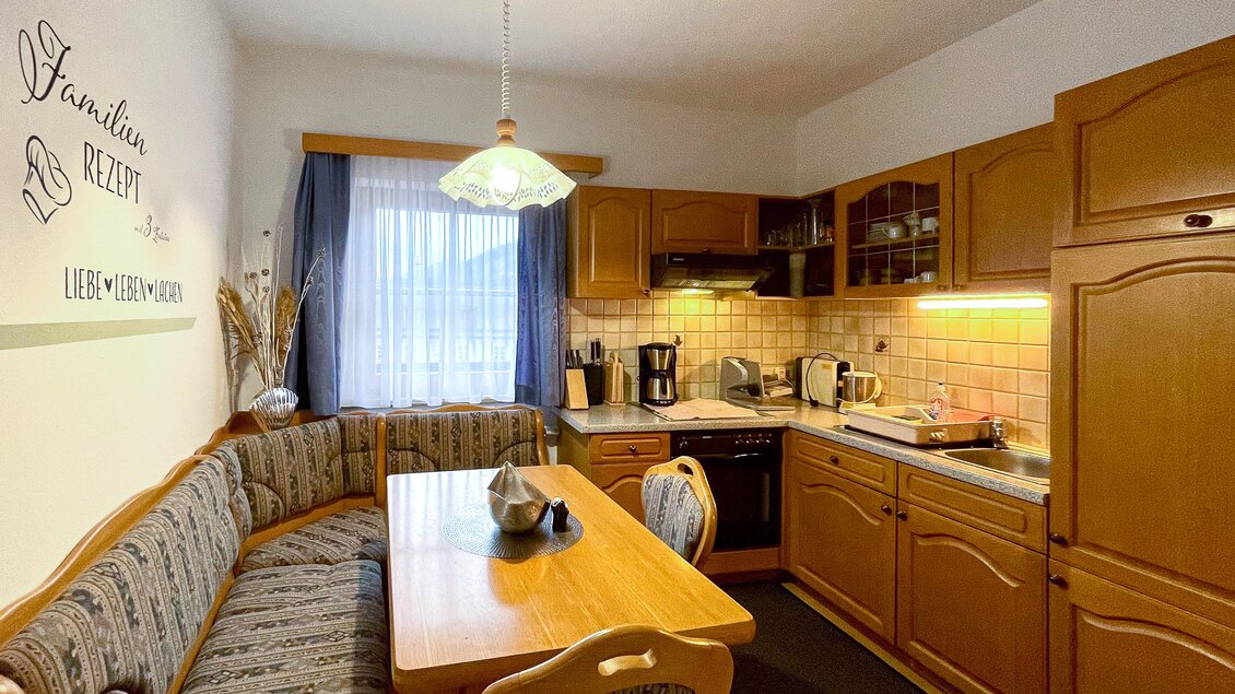 Eine gemütliche Küche mit Holzschränken und einem Essbereich. Die Fenster lassen natürliches Licht herein und die Wände sind dekoriert. | © Gerhard Schernthaner