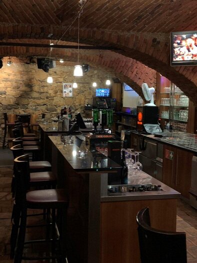 A cozy bar in the basement with stone walls and a long counter. The atmosphere is inviting, with some tables and chairs as well as a TV on the wall. | © Da Nussi, facebook