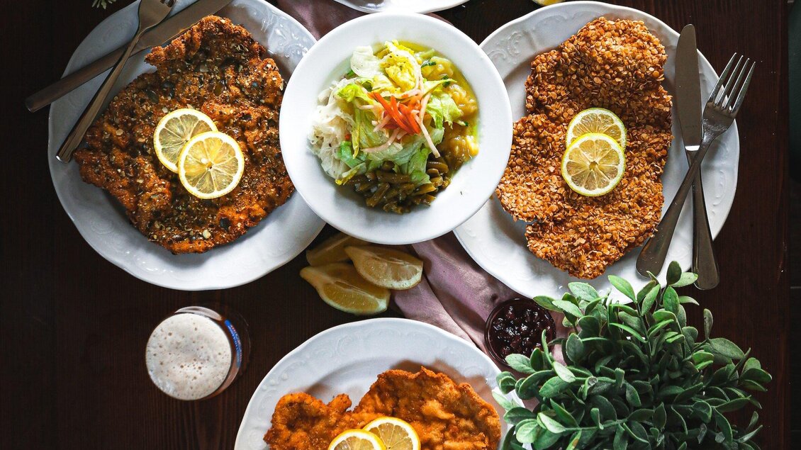 Ein überquellender Tisch mit paniertem Fleisch, garniert mit Zitronenscheiben. Dazu gibt es frischen Salat und ein kühles Getränk. | © 3 Goldene Kugeln