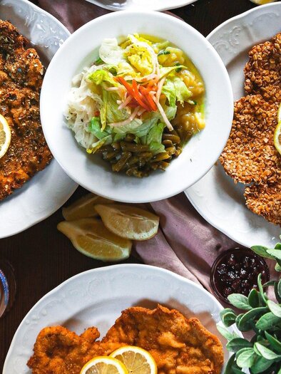 An overflowing table with breaded meat, garnished with lemon slices. Accompanied by fresh salad and a cool drink. | © 3 Goldene Kugeln