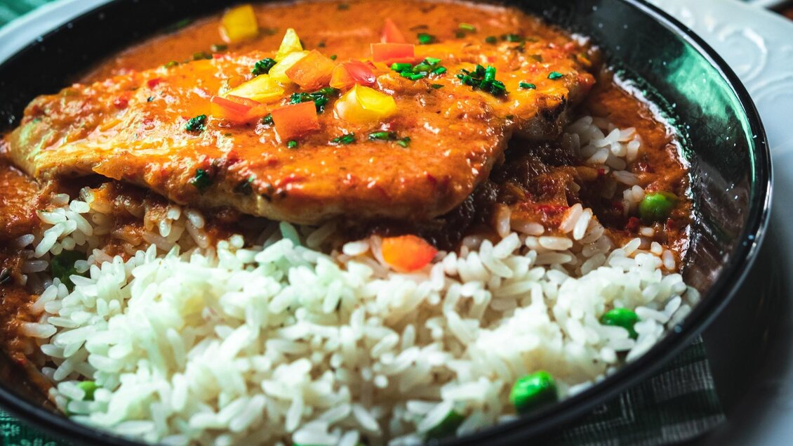 Ein Teller mit Reis und gebratenem Fisch in einer würzigen Sauce. Das Gericht ist mit frischem Gemüse garniert. | © 3 Goldene Kugeln