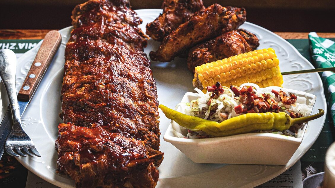 Ein Teller mit saftigen Rippchen, knusprigen Hähnchenflügeln und gegrilltem Mais. Dazu gibt es einen kleinen Salat mit Schoten. | © 3 Goldene Kugeln