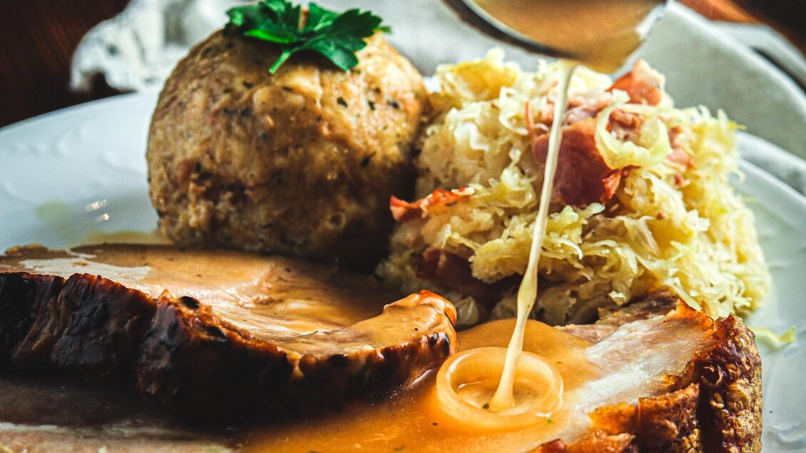 Ein Teller mit saftigem Fleisch, übergossen mit einer Soße. Dazu gibt es Kartoffelknödel und Sauerkraut. | © 3 Goldene Kugeln