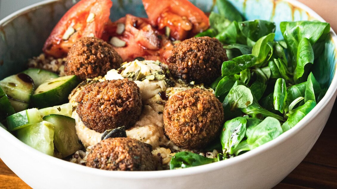Eine bunte Schüssel mit Falafel, frischem Gemüse und grünem Salat. Darin befinden sich auch Hummus und Gurkenscheiben. | © 3 Goldene Kugeln