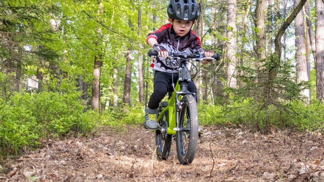Ein Kind fährt Fahrrad auf einem unbefestigten Weg im Wald. Die Umgebung ist grün und bewaldet, ideal für Abenteuer in der Natur. | © 3Eiben Kids Bike-Park