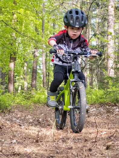 Ein Kind fährt Fahrrad auf einem unbefestigten Weg im Wald. Die Umgebung ist grün und bewaldet, ideal für Abenteuer in der Natur. | © 3Eiben Kids Bike-Park