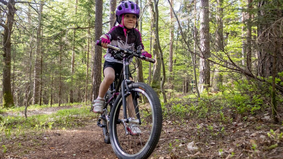 Ein Mädchen mit einem Fahrrad fährt auf einem Waldweg. Umgeben von Bäumen und frischem Grün sieht es abenteuerlich aus. | © 3Eiben Kids Bike Park