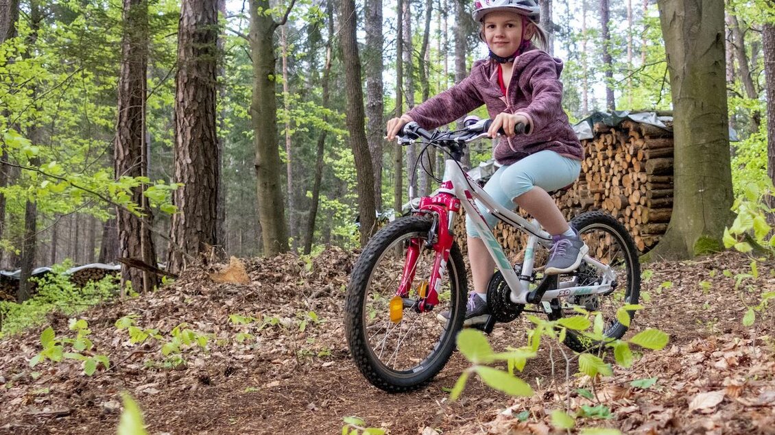 Ein Mädchen fährt auf einem Fahrrad im Wald. Umgeben von Bäumen und frischem Grün, sieht sie glücklich aus. | © 3Eiben Kids Bike Park