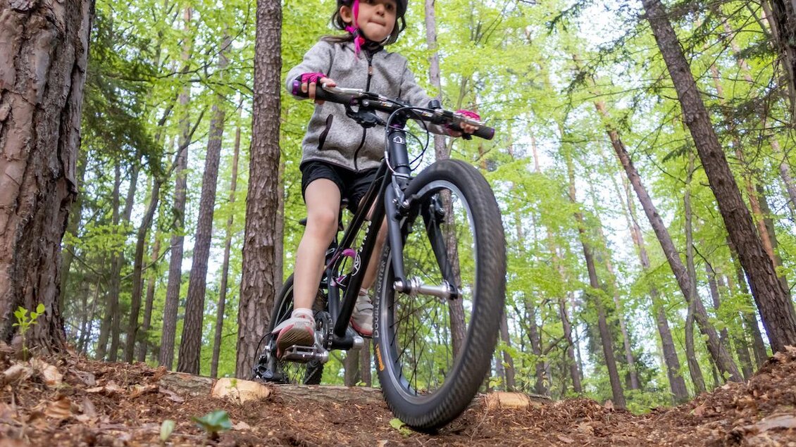 Ein Mädchen fährt Fahrrad auf einem Waldweg. Umgeben von Bäumen und frischem Grün, trägt sie einen Helm und hat Spaß beim Fahren. | © 3Eiben Kids Bike Park